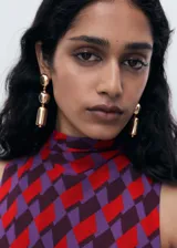 Vestido corto sin mangas con cuello alto, confeccionado en tejido estampado con patrón geométrico en tonos rojos y violetas.
