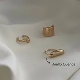 Set de tres anillos dorados de diferentes diseños: un anillo abierto con dos líneas cruzadas, un anillo ancho tipo sello y un anillo con una pieza alargada y redondeada.