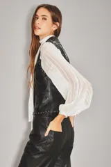 Chaleco de cuero ovino negro con diseño sin mangas, cierre frontal con botones metálicos y detalles de tachas plateadas formando patrones de estrellas en la parte superior delantera.