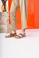 Sandalia negra de plataforma gruesa con dos tiras anchas ajustables con hebilla. Una de las tiras tiene un estampado de vaca blanco y negro.