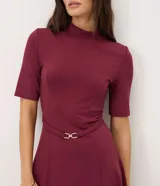 Vestido midi evasé color bordó, con cuello alto, mangas cortas y cintura marcada con cinturón fino removible con hebilla metálica dorada.