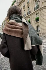 Pañuelo rectangular con diseño color block en tonos beige, gris oscuro y marrón. Presenta una textura tejida y acabados deshilachados en los bordes.