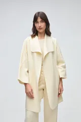 Tapado de largo medio abierto con cuello, confeccionado en lana fina sin teñir con detalles de terminación envivados en los bordes y mangas tres cuartos.