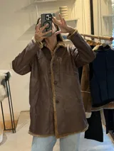 Campera tipo gamulán de cuero genuino con efecto desgastado, cuello de corderito y cierre frontal con botones.