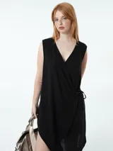 Vestido corto color beige, cruzado, sin mangas y ajustable con lazo lateral.