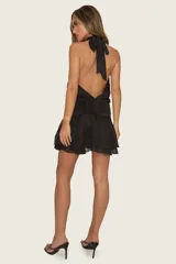 Vestido corto negro con cuello halter, espalda descubierta y falda de volados, confeccionado en tela liviana con cintura elastizada.