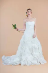 Vestido de novia blanco de organza, con corset drapeado, falda con volados y cola larga. Presenta un delicado bordado de perlas en la cintura.