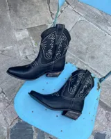 Botas estilo texanas de cuero vacuno color negro, con costuras decorativas en contraste de color blanco. Presentan punta fina y taco cuadrado de madera.