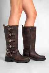 Borcegos de caña alta confeccionados en cuero sintético con acabado envejecido. Presentan múltiples hebillas metálicas decorativas a lo largo del lateral y una correa ajustable con hebilla doble en la zona del tobillo. Cuentan con suela de goma negra con plataforma y cierre lateral.