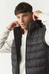 Chaleco negro acolchado con capucha ajustable, cierre frontal y bolsillos laterales con cierre. Logo de la marca en el pecho. Colección Otoño Invierno 2025. El modelo usa talle M. Composición 100% nylon.