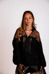 Camisa negra de manga larga con detalles de encaje en hombros y puños. Presenta un cuello tipo solapa y cierre frontal con botones dorados.