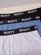 Pack de tres bóxers Rusty con banda elástica negra con el logotipo de la marca impreso en blanco. Incluye modelos en color negro, celeste y gris melange.