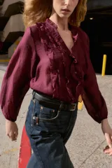 Blusa de escote en pico con volantes decorativos, manga larga con puños elásticos y cierre frontal con botones.