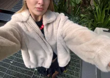 Chaqueta de textura suave tipo peluche, color beige, con cierre frontal metálico, cuello alto, bolsillos laterales y ruedo con elástico regulable.