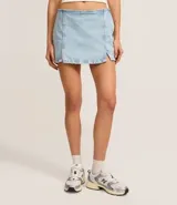 Short pollera de jeans celeste claro, tiro bajo, con ruedo deshilachado y un tajo lateral con detalle de encaje blanco en el borde.
