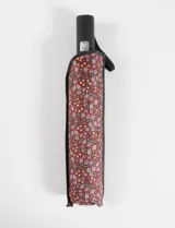 Paraguas plegable automático con funda protectora estampada con diseño floral en tonos rojos, blancos y amarillos. Cuenta con mango ergonómico negro y correa de sujeción.