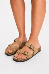 Sandalia plana de color tostado con diseño de tiras cruzadas y doble tira superior con hebillas metálicas ajustables, plantilla estilo corcho y suela negra.