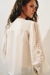 Camisa de organza de viscosa color crudo, con cuello subido, escote en V y manga larga. Presenta detalles de bordados florales en contraste a lo largo del frente y cierre frontal con botones.
