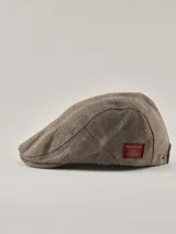 Boina de estilo clásico en color visón con patrón de espiga sutil. Presenta una etiqueta rectangular roja con el logo de la marca en el lateral.
