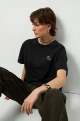 Remera negra de corte oversize con cuello redondo y manga corta. Presenta un pequeño estampado dorado en el pecho con la frase "love earth" y un símbolo de hojas.