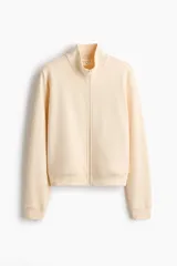 Campera deportiva de felpa de algodón color beige, de corte ajustado, con cuello elevado, cierre frontal y bolsillos laterales discretos. Presenta puños y bajo acanalados.