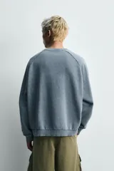 Sudadera de corte relaxed fit confeccionada en tejido de algodón con interior de rizo. Presenta cuello redondo, manga larga y acabados en rib, con un acabado de efecto lavado que le otorga una apariencia única.