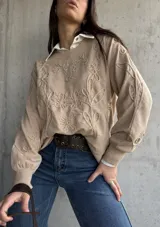 Sweater de punto color beige con diseño bordado en relieve de flores y hojas. Presenta cuello redondo, mangas largas con puños acanalados y un corte holgado.