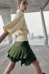 Falda corta de satén color verde oliva, con cintura fruncida y dos niveles de volantes con terminación ondulada.