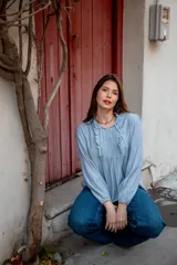 Camisa de color celeste con volados decorativos en el cuello y la parte delantera, cuenta con cordones para ajustar el escote, mangas largas con puños y corte holgado.