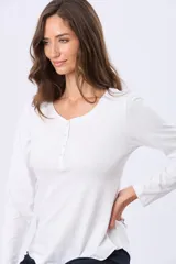 Remera lisa de algodón color blanco, con cuello redondo y botones a tono. Tiene manga larga y un ruedo curvo.