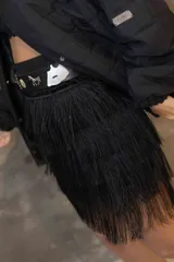 Pollera corta negra de rafia cubierta de flecos en capas. Se complementa con un cinturón negro con apliques metálicos.