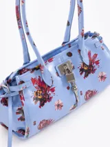 Cartera de hombro de cuero vacuno color celeste con estampado floral multicolor. Cuenta con cierre superior, bolsillo interno, asas largas y detalles de herrajes metálicos con candado y llavero colgante en el frente.