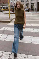 Top de punto color verde militar, con cuello subido y manga sisa. Presenta apliques dorados en los laterales y un bajo asimétrico.