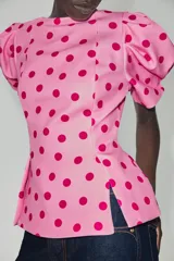 Top rosado con estampado de lunares fucsia, de cuello redondo y mangas cortas abullonadas con pliegues. Cuenta con escote en V en la espalda y cierre con cremallera oculta.