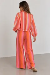 Pantalón de tiro alto y pierna ancha con estampado de rayas verticales en tonos rosados, naranjas y marrones. Cuenta con cintura elástica con cordón de ajuste y bolsillos laterales.