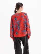 Buzo de algodón con cuello redondo y mangas largas, estampado con diseño de flores y alfileres de gancho sobre fondo rojo. Presenta puños y ruedo en tejido elástico al tono.