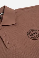 Polo de manga larga en tejido texturado color marrón, con cuello estructurado, cierre frontal de botones y detalle gráfico bordado en el pecho.