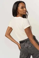 Remera de manga corta color blanco roto, con cuello redondo y calce ajustado tipo baby tee. Estampado frontal con el texto "TEAM NAUGHTY" en letras rojas y verdes.