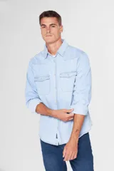 Camisa de jean celeste de manga larga, con cuello clásico, cierre frontal con botones a presión, dos bolsillos con solapa abotonada en el pecho, corte en hombros y detalle en la espalda.