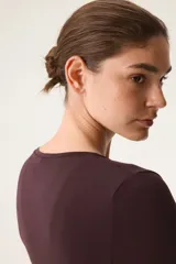 Top deportivo de manga larga confeccionado en modal suave de color bordó, con diseño cruzado, escote en V pronunciado, tiras para anudar en la cintura y corte ajustado.