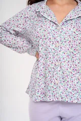 Pijama de dos piezas, compuesto por una camisa de manga larga con botones y cuello clásico, estampada con flores pequeñas en tonos lila y verde sobre fondo blanco, y un pantalón liso color lila con cintura elástica.