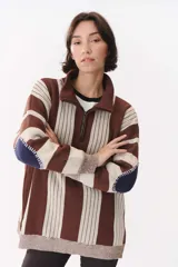 Buzo de tejido de punto con diseño de rayas verticales en tonos bordó y rojo. Presenta cuello alto con cierre frontal, mangas largas con coderas en contraste y detalles de costuras visibles.