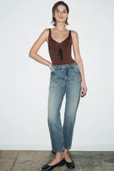 Jeans de tiro medio con corte slim leg, confeccionados en denim color beige. Presentan cintura con trabillas, diseño clásico de cinco bolsillos y cierre frontal con cremallera y botón metálico.