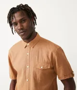 Camisa de hombre de manga corta color marrón, confeccionada en lino y algodón. Presenta cuello clásico, botonadura frontal, bolsillo en el pecho y mangas con botón para enrollar.