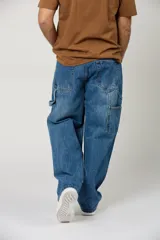 Jean de corte baggy con diseño carpintero, confeccionado en denim azul clásico. Presenta un ajuste holgado, tiro medio y bolsillos laterales utilitarios característicos del estilo carpintero.