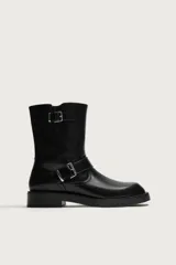 Bota de media caña color negro con horma cuadrada, suela con ligero tacón y ajuste mediante dos tiras con hebilla metálica, una en el empeine y otra en la parte superior de la caña.
