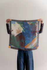 Pañuelo cuadrado de seda con diseño estampado tipo patchwork que combina motivos botánicos, arquitectónicos y geométricos en tonos azules, verdes, ocres y crema, con un borde a rayas multicolor.