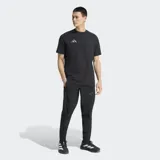 Pantalón deportivo Adidas del Real Madrid, modelo Tiro Travel, color negro. Presenta un diseño técnico con corte clásico, cintura elástica, costuras ergonómicas para mayor movilidad y bolsillos laterales. Incluye el escudo del club y el logo de la marca en tono sobre tono.