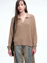 Sweater de tejido de punto color beige, con diseño de trenzas en el frente y mangas lisas. Presenta cuello polo con escote en V y puños y ruedo acanalados.