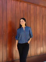 Camisa de jean azul con cuello mao, cierre frontal con botones rojos y mangas tres cuartos abullonadas con puños elásticos.